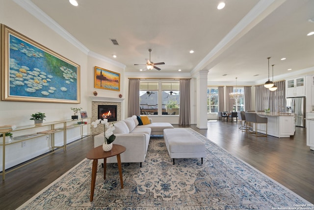 living room featuring visible vents, dark wood finished floors, a glass covered fireplace, crown molding, and ornate columns