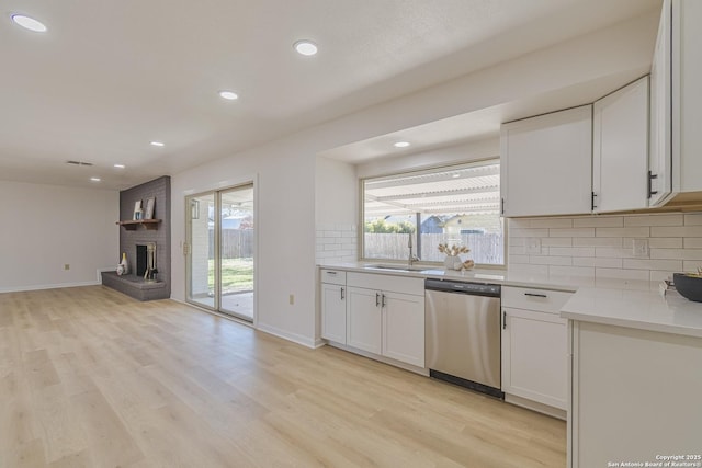 kitchen featuring stainless steel dishwasher, decorative backsplash, light wood-style flooring, and a healthy amount of sunlight