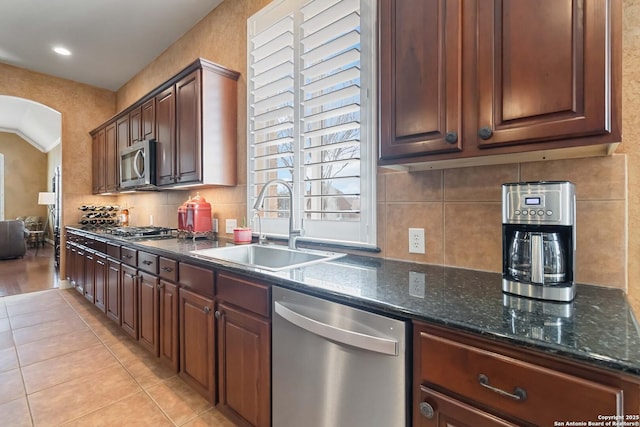 kitchen with arched walkways, light tile patterned floors, a sink, appliances with stainless steel finishes, and backsplash