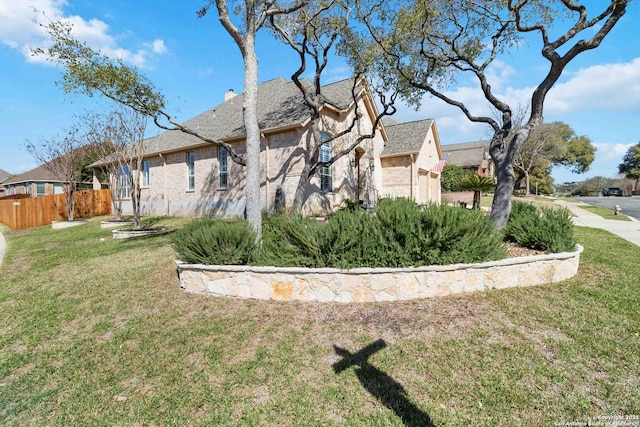 view of side of home featuring an attached garage, brick siding, fence, a yard, and a chimney