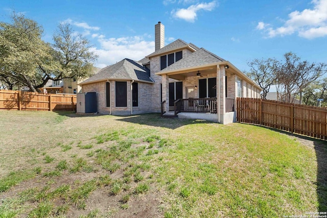 back of house featuring a yard, brick siding, a chimney, and a fenced backyard