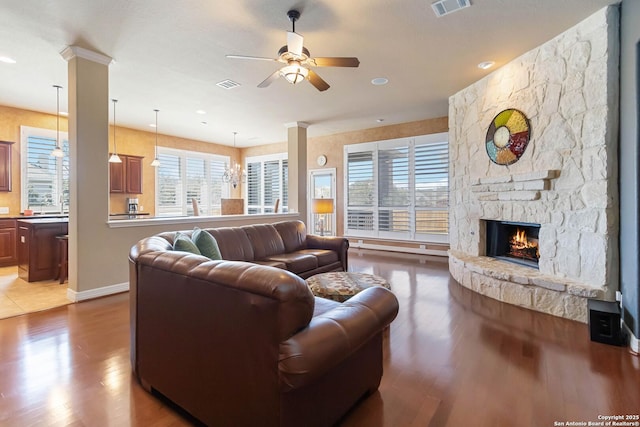 living area with ceiling fan, a fireplace, wood finished floors, visible vents, and ornate columns