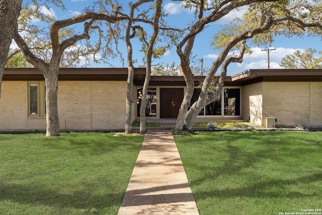 mid-century inspired home featuring brick siding, central AC, and a front lawn