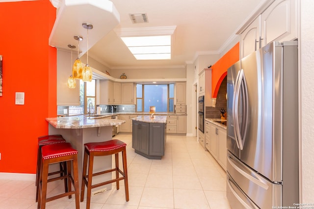 kitchen featuring a peninsula, visible vents, a kitchen breakfast bar, freestanding refrigerator, and crown molding