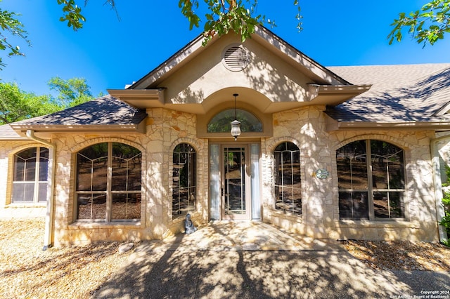 entrance to property with stone siding and roof with shingles