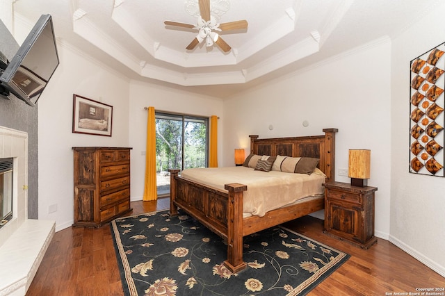 bedroom with access to exterior, a raised ceiling, a tiled fireplace, dark wood-type flooring, and ornamental molding