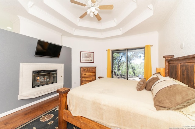 bedroom featuring a raised ceiling, ornamental molding, a glass covered fireplace, wood finished floors, and access to outside