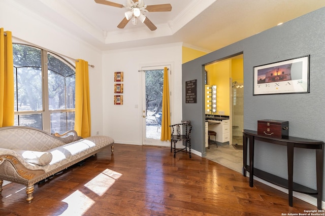 living area with baseboards, a raised ceiling, a ceiling fan, ornamental molding, and wood finished floors