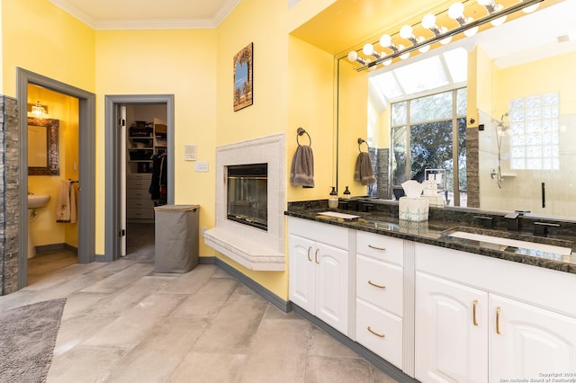 bathroom featuring double vanity, a glass covered fireplace, an enclosed shower, crown molding, and a sink