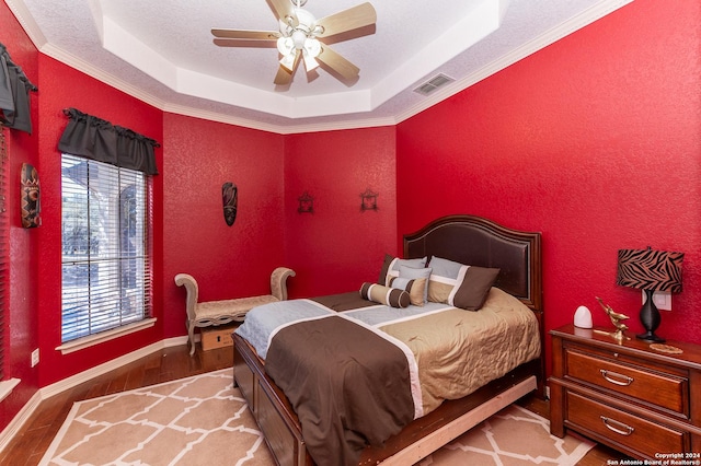 bedroom with a textured wall, a tray ceiling, light wood-style flooring, and visible vents