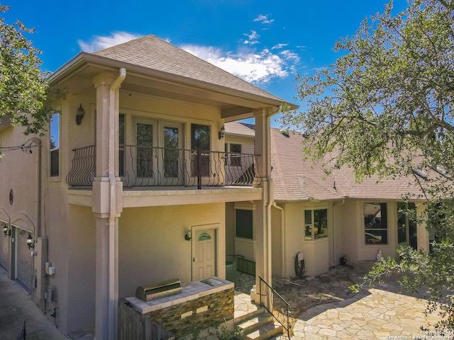 rear view of property with a balcony, a shingled roof, and stucco siding