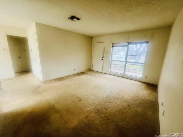 unfurnished room with a textured ceiling, visible vents, and light colored carpet