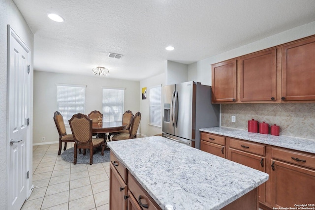 kitchen featuring light tile patterned flooring, a kitchen island, decorative backsplash, brown cabinets, and stainless steel fridge