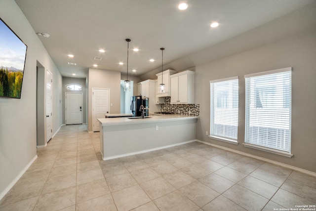 kitchen with a sink, tasteful backsplash, a peninsula, white cabinets, and light countertops