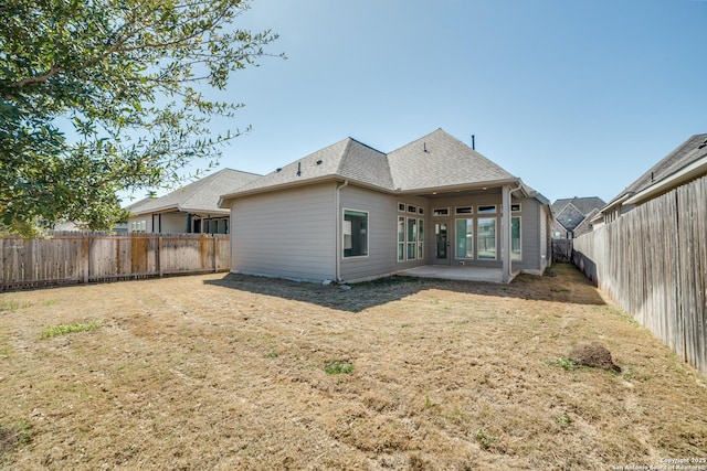 rear view of property featuring a patio, a yard, a fenced backyard, and roof with shingles