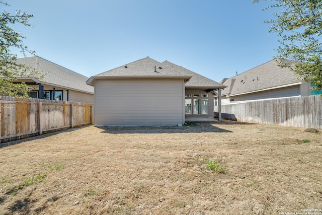 back of property with a lawn, a fenced backyard, and roof with shingles