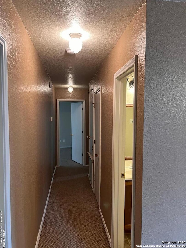 hallway featuring a textured ceiling, a textured wall, carpet flooring, and baseboards