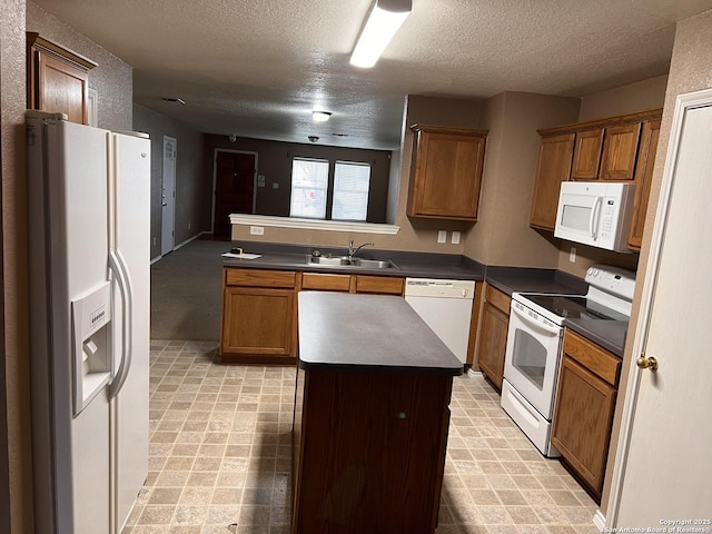 kitchen with a peninsula, white appliances, a kitchen island, a sink, and dark countertops