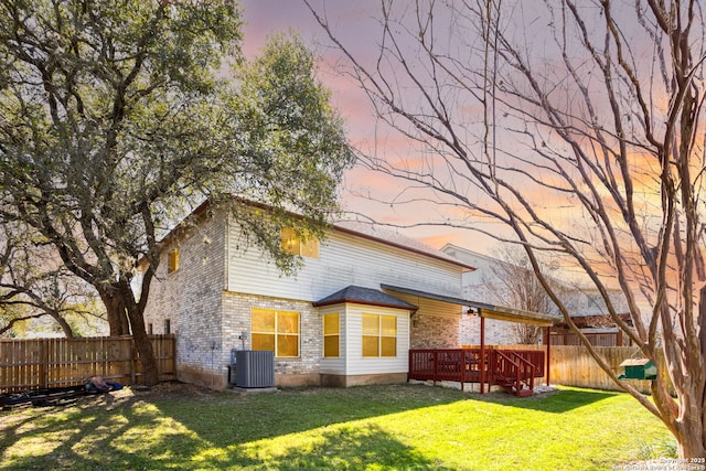 back of house featuring a lawn, a fenced backyard, a wooden deck, central air condition unit, and brick siding