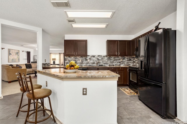 kitchen featuring black appliances, a breakfast bar area, visible vents, and a center island