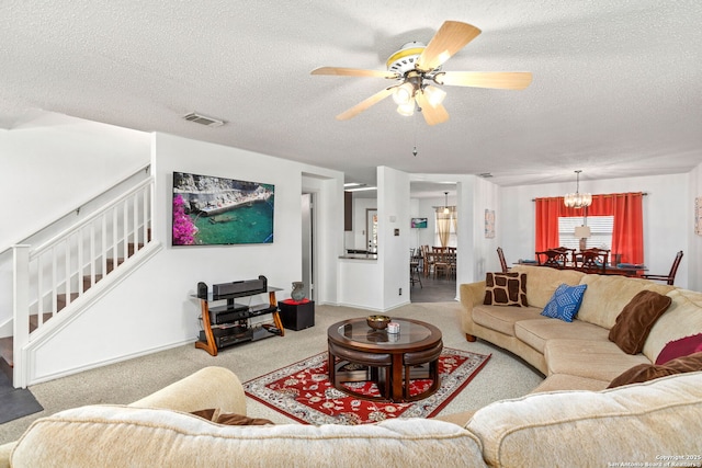 carpeted living room featuring a textured ceiling, stairway, ceiling fan with notable chandelier, and visible vents