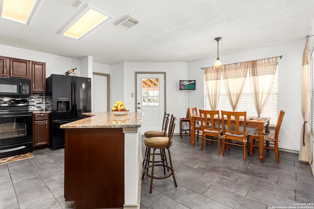 kitchen with a kitchen island, visible vents, black appliances, tasteful backsplash, and a kitchen bar