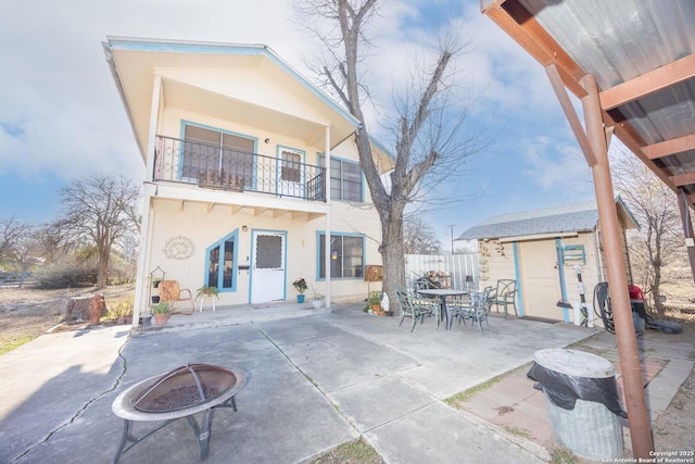 back of house featuring a balcony, an outdoor structure, stucco siding, a storage unit, and a patio area