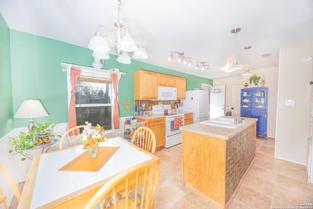 kitchen featuring a kitchen island with sink, white appliances, a sink, backsplash, and an inviting chandelier