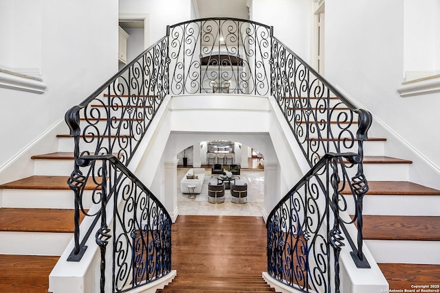 stairway featuring arched walkways, a high ceiling, and wood finished floors