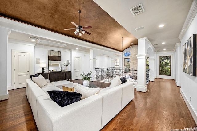 living room featuring wood finished floors, visible vents, baseboards, decorative columns, and crown molding