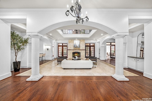 living room featuring decorative columns, arched walkways, wood finished floors, crown molding, and a fireplace