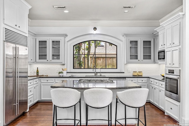 kitchen featuring built in appliances, dark wood-type flooring, a kitchen island, and a kitchen bar