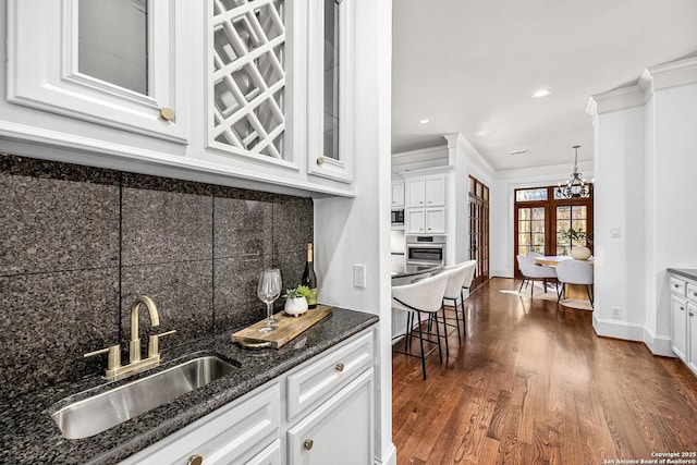 kitchen with tasteful backsplash, white cabinets, ornamental molding, oven, and a sink