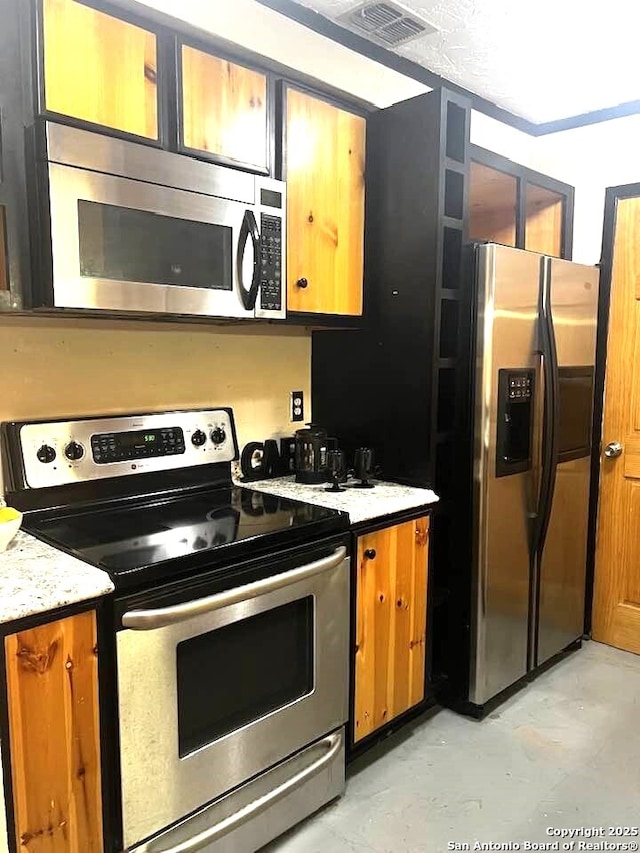 kitchen featuring concrete flooring, appliances with stainless steel finishes, brown cabinetry, and visible vents