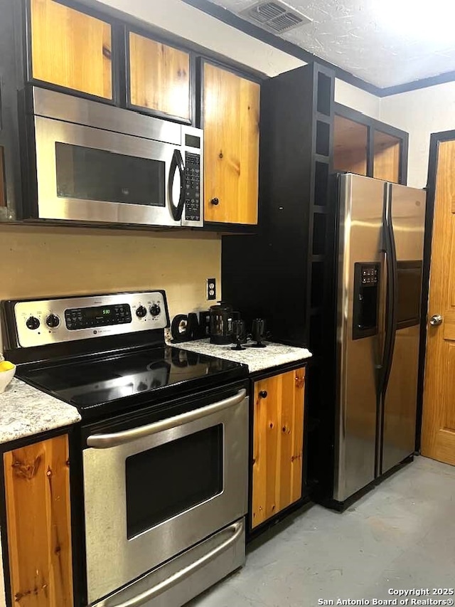 kitchen with concrete flooring, light stone counters, visible vents, appliances with stainless steel finishes, and brown cabinets