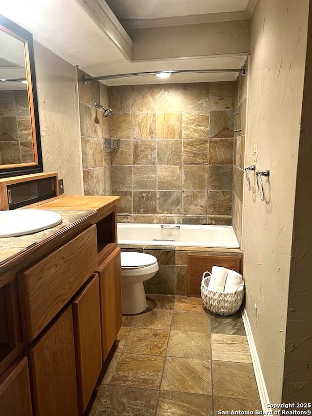 full bathroom with tiled shower / bath, stone tile floors, a textured wall, toilet, and vanity