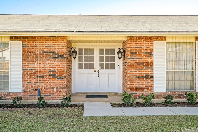 entrance to property with brick siding and a shingled roof