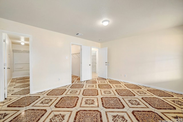 unfurnished bedroom with a walk in closet, a closet, visible vents, ensuite bathroom, and baseboards