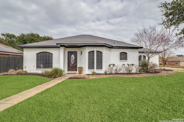 view of front of house with roof with shingles, brick siding, a front lawn, and fence