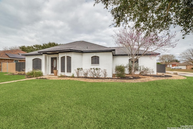 view of front of home featuring a shingled roof, brick siding, fence, and a front lawn