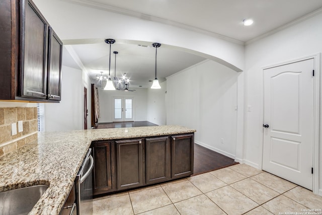 kitchen with arched walkways, light tile patterned floors, dark brown cabinetry, a peninsula, and ornamental molding