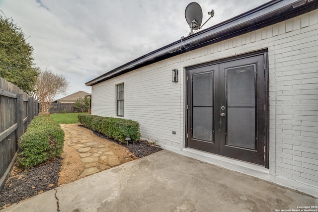 view of exterior entry with a patio area, fence, french doors, and brick siding