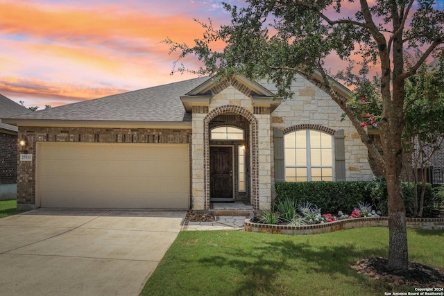 french country style house featuring roof with shingles, an attached garage, a front yard, stone siding, and driveway