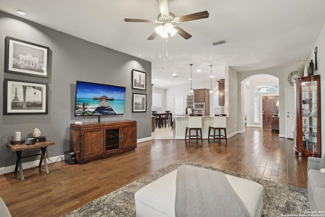 living room with arched walkways, dark wood-type flooring, visible vents, and baseboards