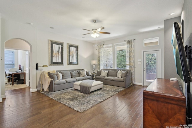 living room featuring dark wood-type flooring, arched walkways, ceiling fan, and baseboards