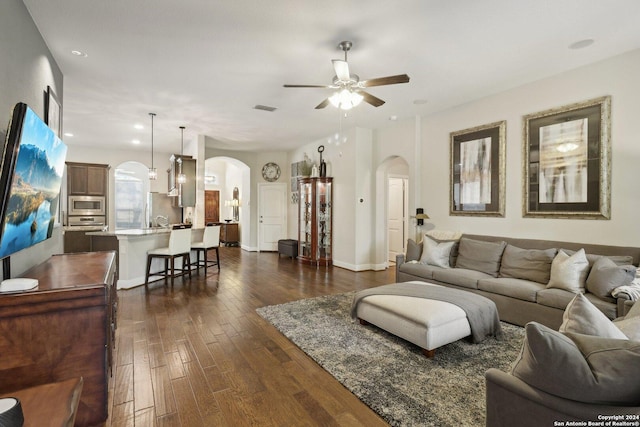 living area featuring arched walkways, dark wood-style flooring, visible vents, a ceiling fan, and baseboards