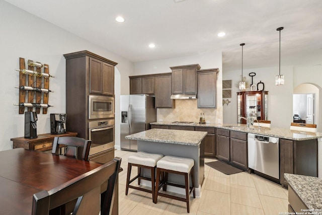 kitchen featuring light stone counters, a sink, stainless steel appliances, dark brown cabinets, and backsplash