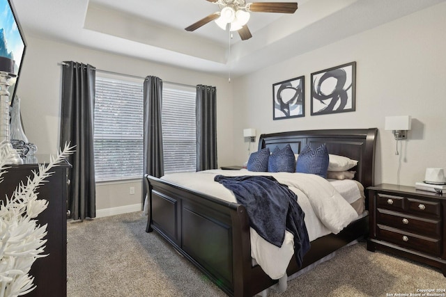 carpeted bedroom with ceiling fan, a raised ceiling, and baseboards