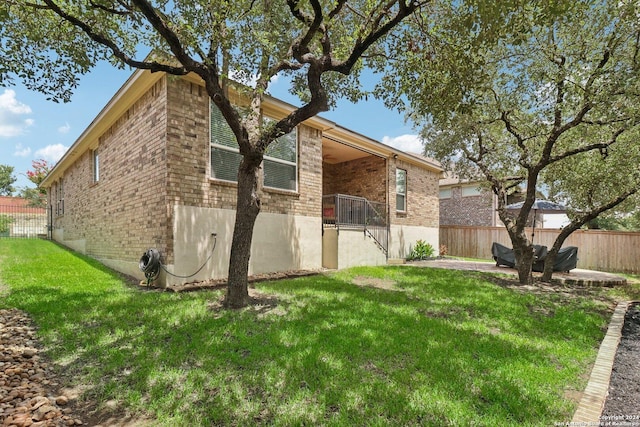 view of side of home with a patio, fence, a lawn, and brick siding