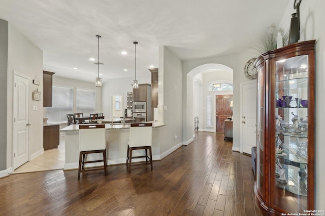 kitchen featuring arched walkways, hardwood / wood-style flooring, stainless steel appliances, a peninsula, and a kitchen bar